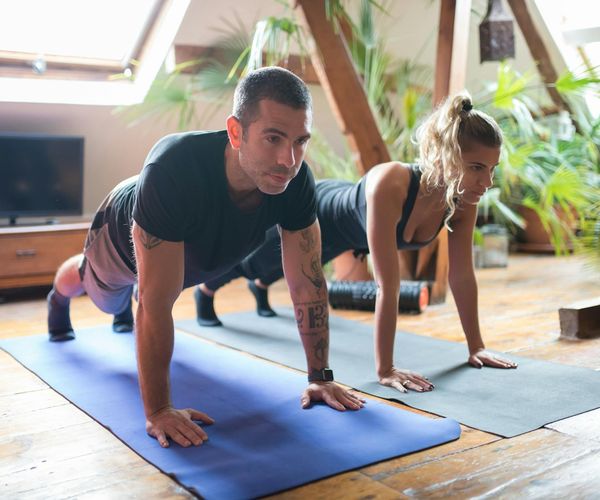 Man performing a deep stretching yoga pose on a mat in a bright room.